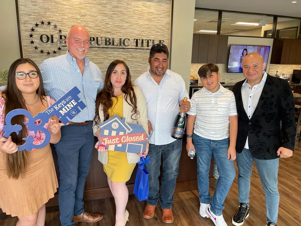 A family celebrating on closing day at the title company, holding “Just Closed” and “The Keys are MINE” signs.
